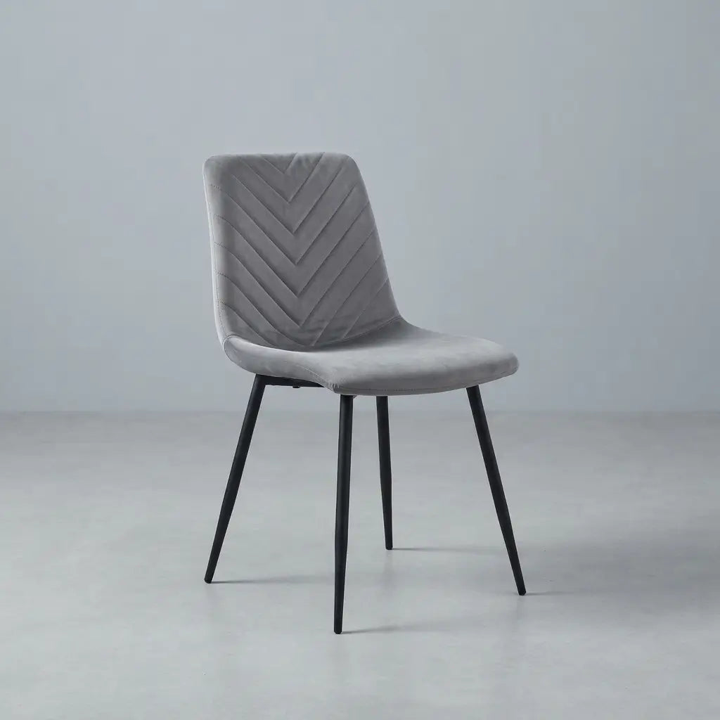 A modern gray upholstered dining chair with a chevron-patterned backrest and slim black metal legs, shown against a minimalist light gray studio background.