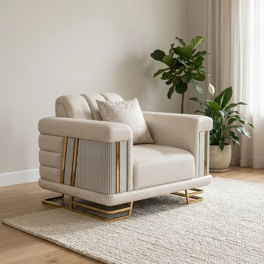 A modern beige armchair with gold metal accents and a textured throw pillow, styled in a minimalist living room setting on a light rug with potted plants in the background.