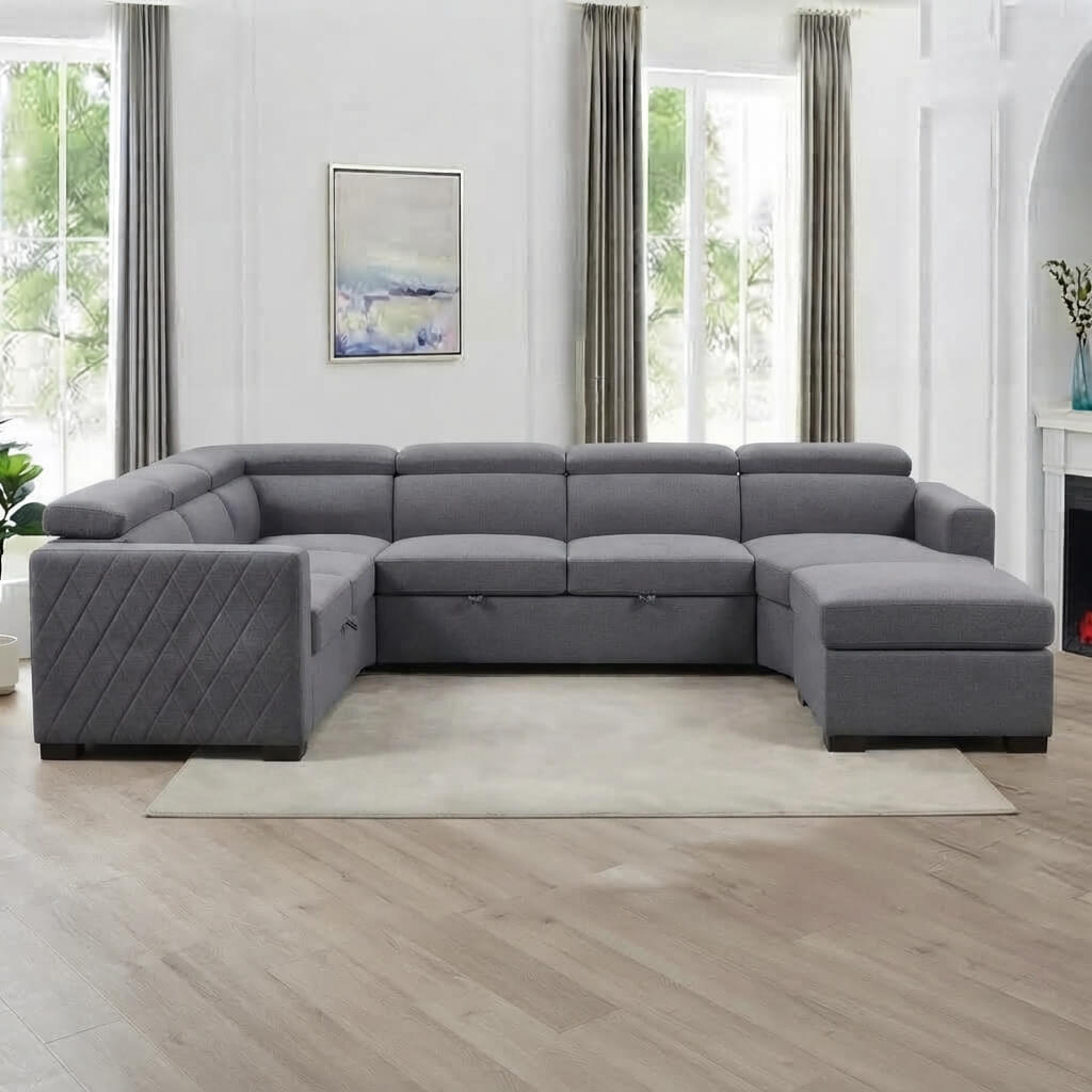 A large gray upholstered sectional sofa with a right-facing chaise ottoman, shown in a bright modern living room with light wood floors, gray curtains, and a white wall.