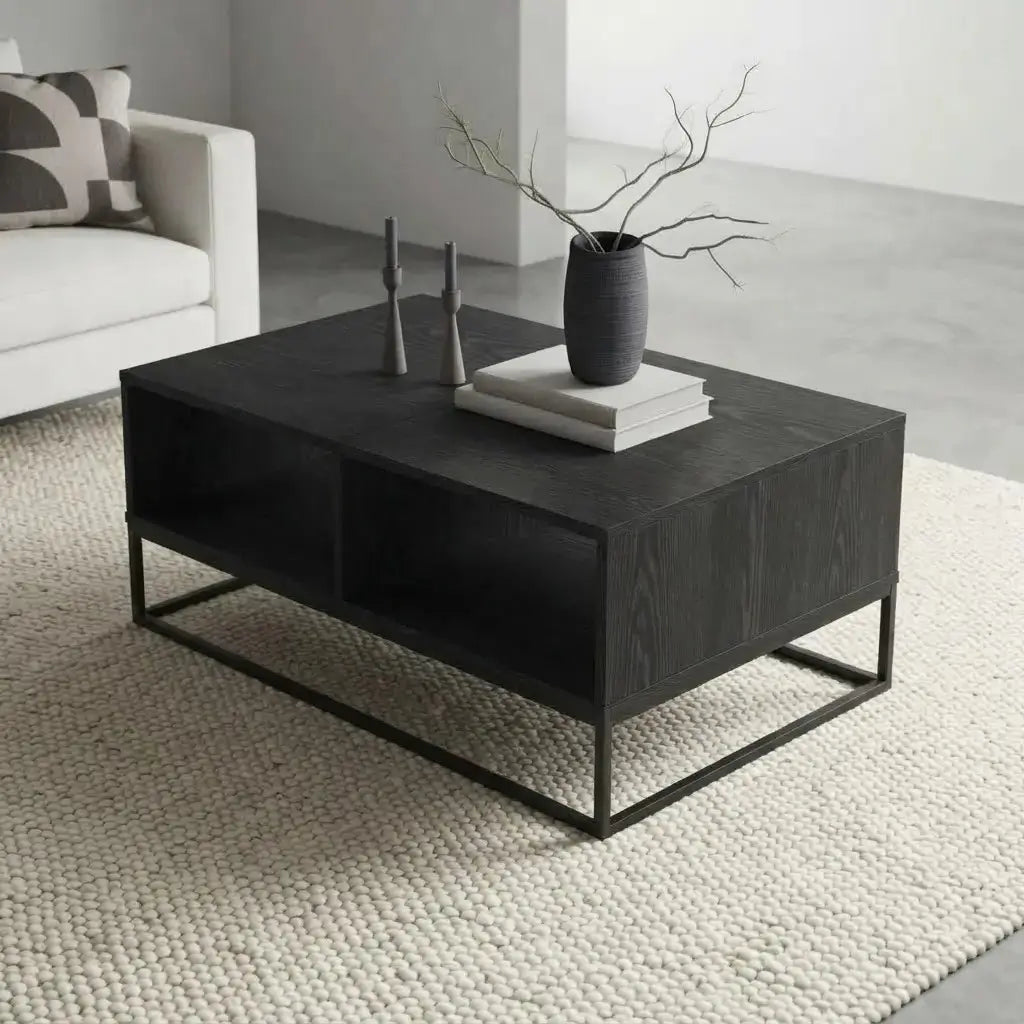 A modern rectangular coffee table with a dark wood grain finish and a black metal frame, styled in a minimalist living room setting with a textured cream rug, a white sofa, and decorative objects on top.