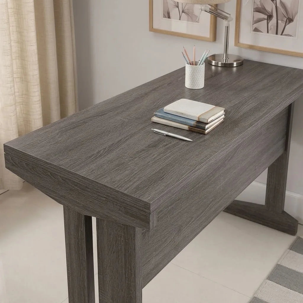 Front eye-level shot of a dark grey wooden study desk styled with a desk lamp, picture frames, and a wicker storage basket underneath.