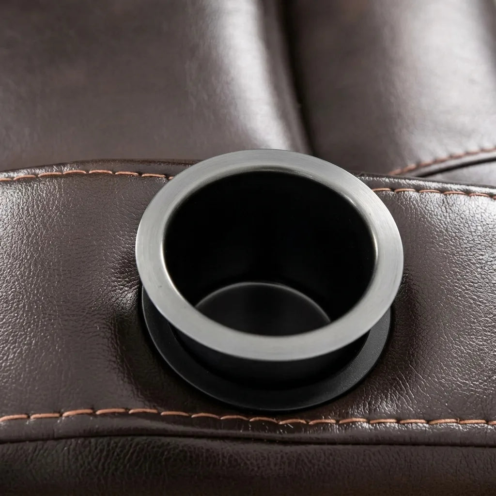 Close-up shot of a black integrated cup holder with a brushed metal trim ring built into the dark brown leather armrest of a recliner chair.