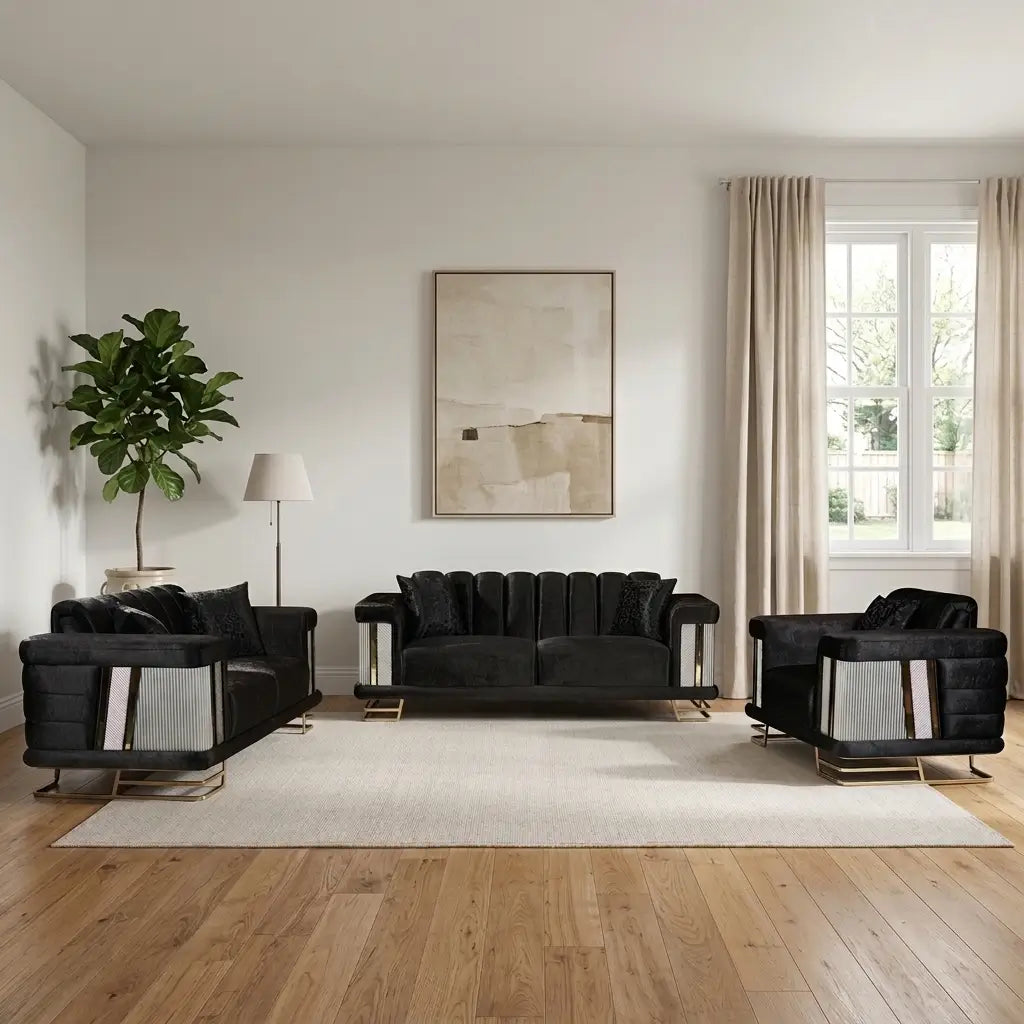 A modern living room set featuring a black velvet sofa, matching armchair, and side table with silver geometric side panels and gold legs, arranged on a light beige rug over a wood floor. The room has white walls, beige curtains, a potted plant, and a minimalist framed art piece.
