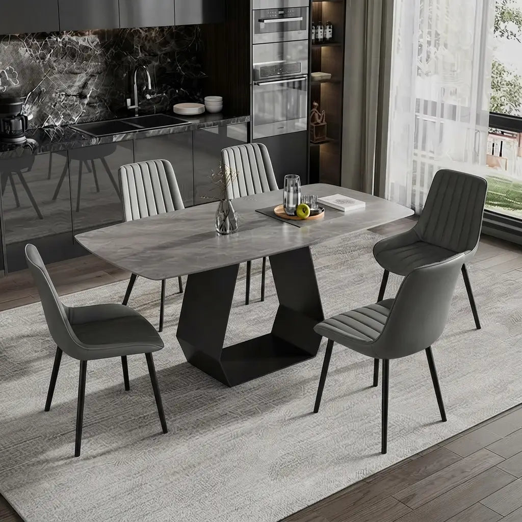A modern dining set featuring a rectangular gray stone-look table with a sculptural black base, surrounded by four gray upholstered chairs with black legs, set on a light gray rug in a contemporary kitchen interior.