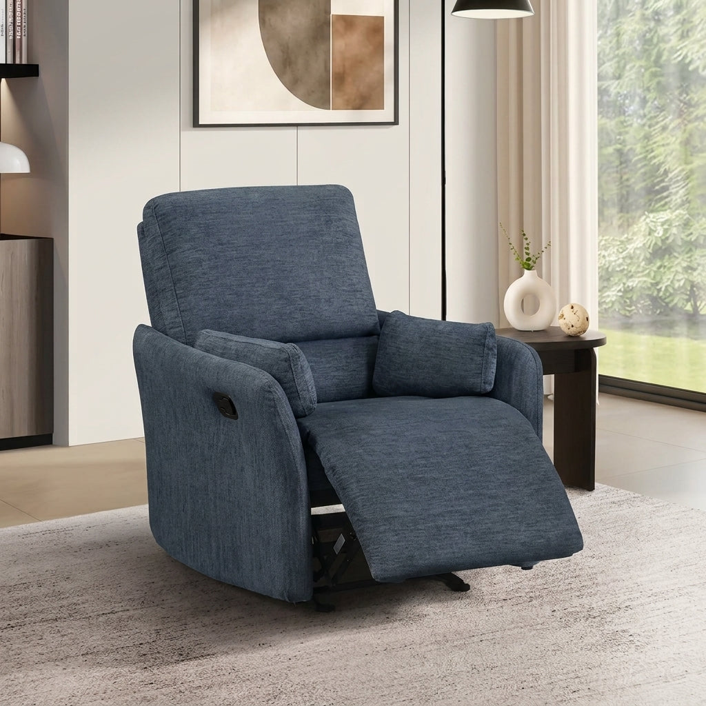 A slightly angled side profile of a modern, upholstered push-back recliner in a textured blue fabric. It is featured in a warm, neutral room on a speckled rug, next to a small side table and a large window.
