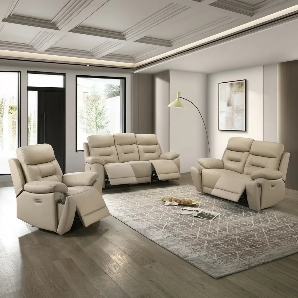 A photorealistic image of a three-piece power reclining living room set in light beige leather. The set, arranged on a geometric-patterned gray rug over light wood floors, includes a single armchair recliner (far left), a three-seater sofa recliner (center-back), and a two-seater loveseat recliner (right). All pieces have their power-reclining footrests extended. To the right of the central sofa is a gold-finished arc lamp over a small side table. In the background, there is a large window and framed art on