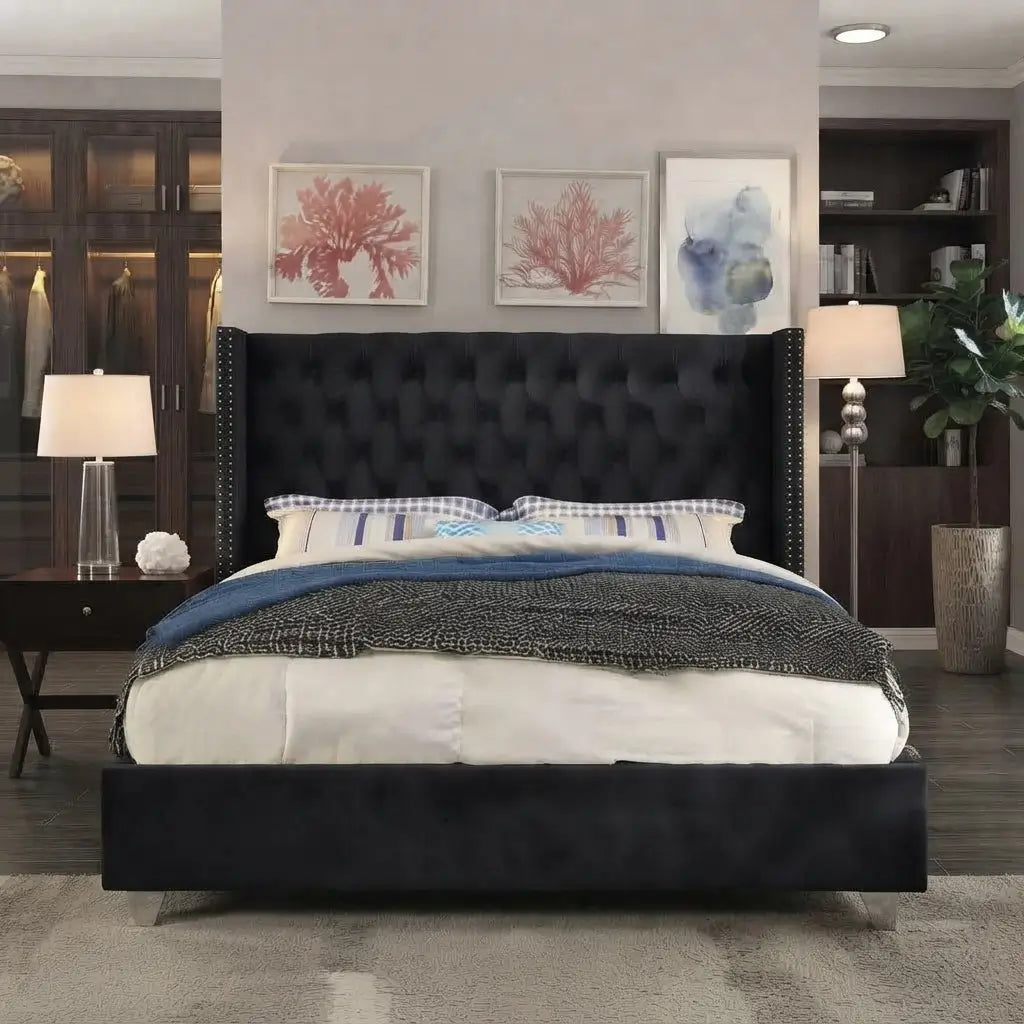 A black upholstered bed frame with a tall tufted headboard and nailhead trim, shown in a styled bedroom setting with white bedding, blue accents, framed wall art, and dark wood furniture.