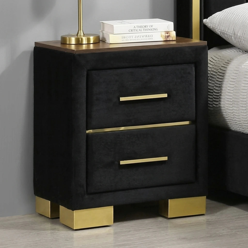 Close-up of a 2-drawer black velvet nightstand with polished gold feet, gold drawer pulls, and a dark wood top surface