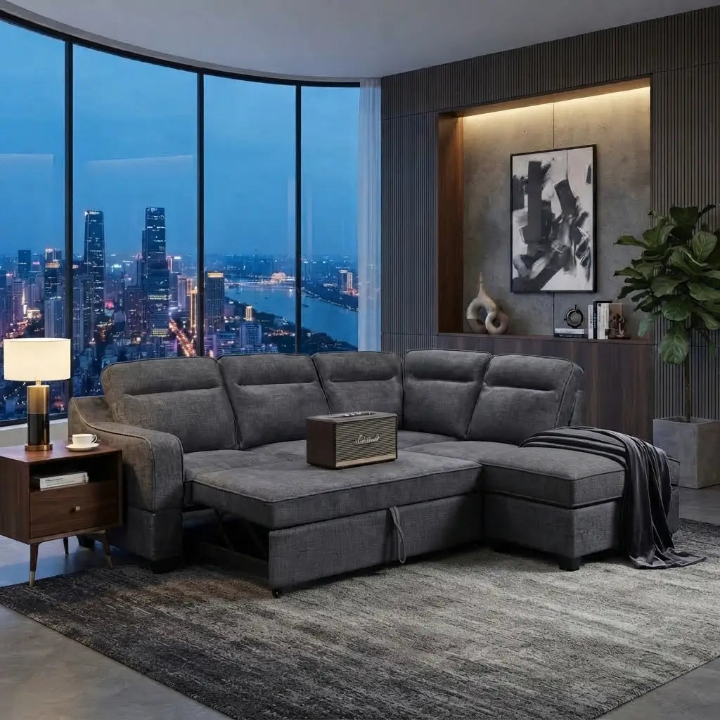 A modern L-shaped sectional sofa in textured gray fabric, styled in a contemporary living room with a large window overlooking a city skyline at dusk. A small speaker sits on the sofa, and a dark throw blanket is draped over the chaise.